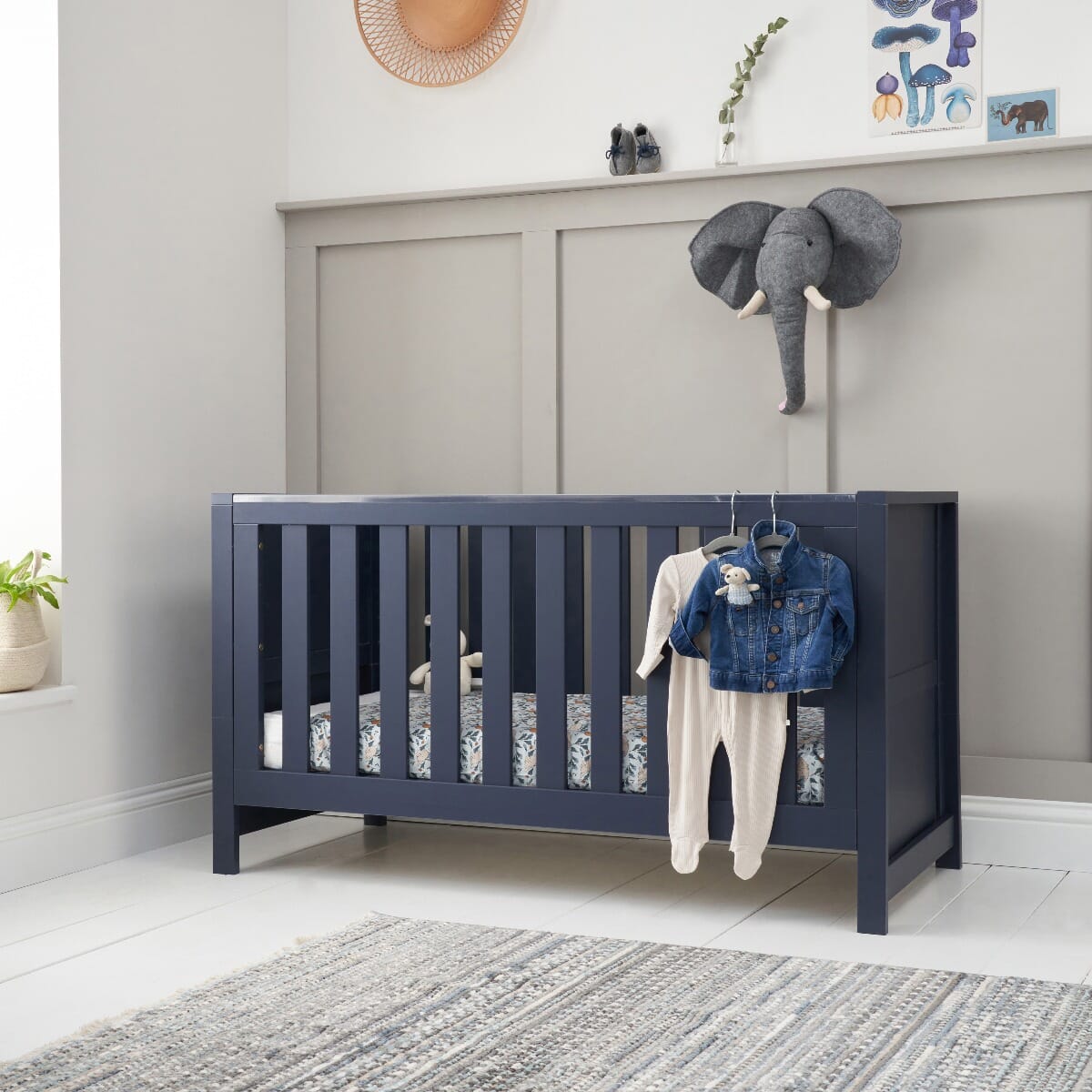 Tivoli cot bed in navy styled in a modern nursery, with soft bedding and clothes on display to show its versatile, practical design