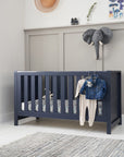 Tivoli cot bed in navy styled in a modern nursery, with soft bedding and clothes on display to show its versatile, practical design