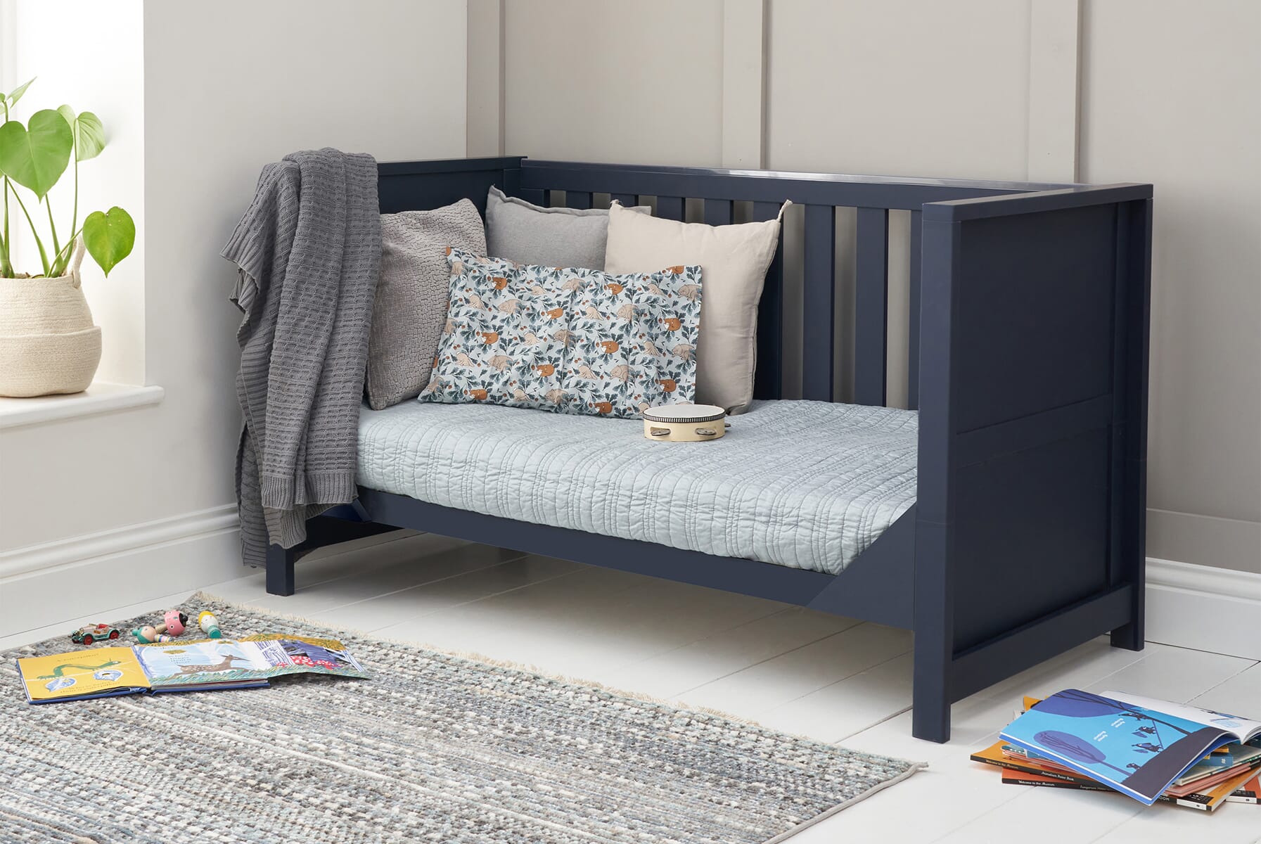Tivoli cot bed in navy shown in sofa bed mode, styled with cushions and blankets to create a cosy reading and relaxation space