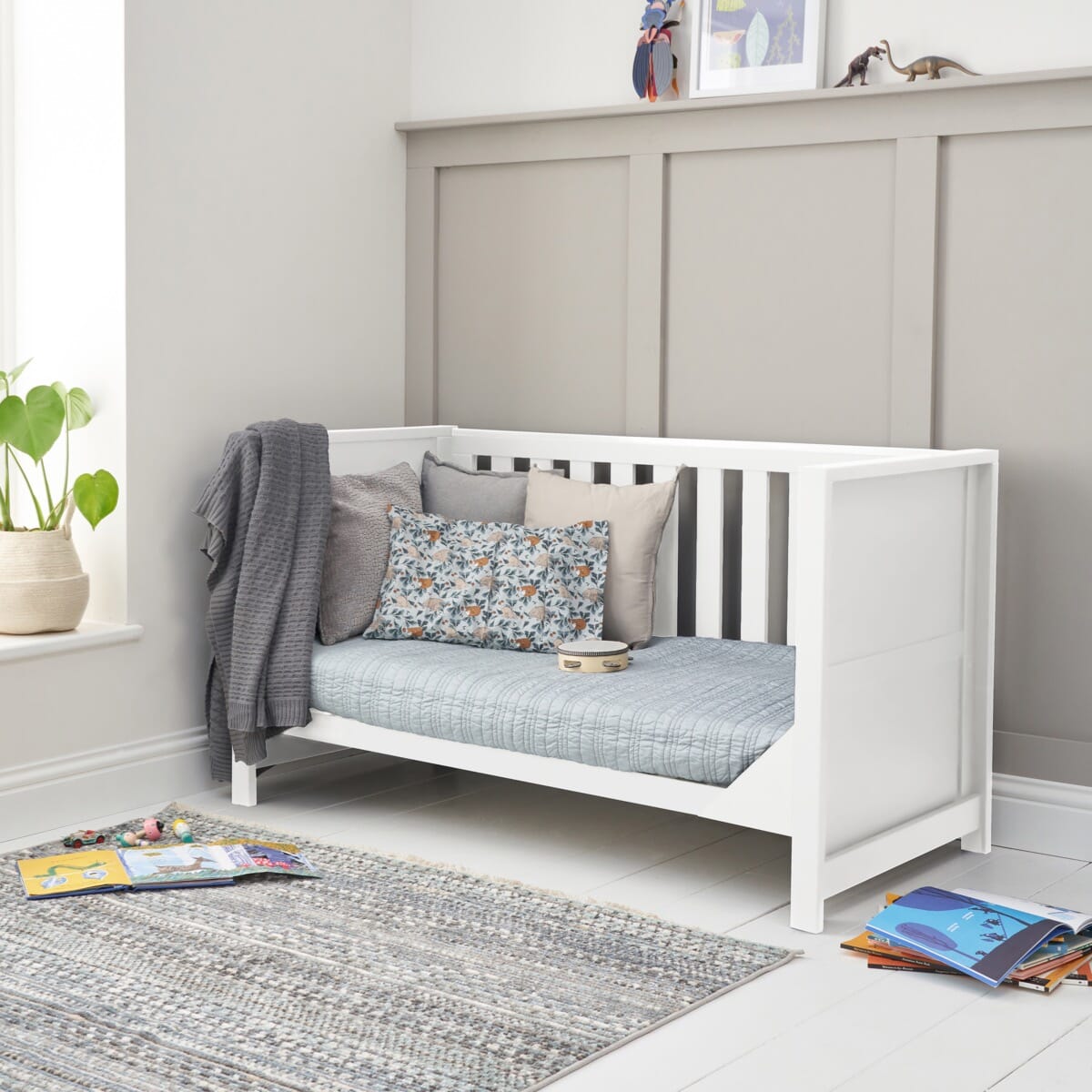 Tivoli cot bed in white shown in sofa bed mode, styled with cushions and soft textiles in a calm playroom setting with natural light