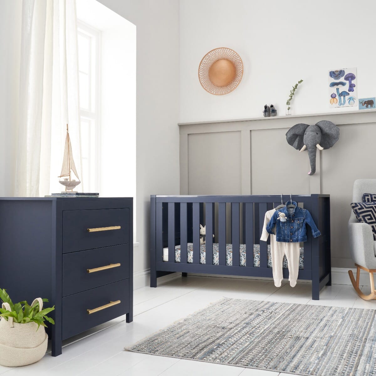 Lifestyle view of the Tivoli cot bed and chest changer in navy, styled with soft toys and wall decor to show a calm, coordinated nursery setup