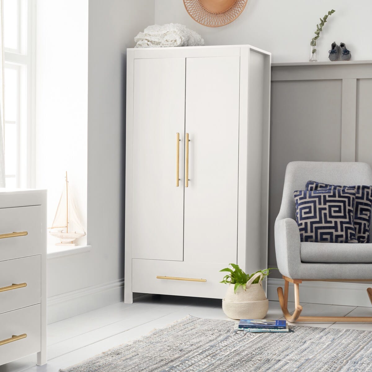 A white Tivoli wardrobe with gold handles is situated in a room with a grey chair, wooden floor, and decorative items.