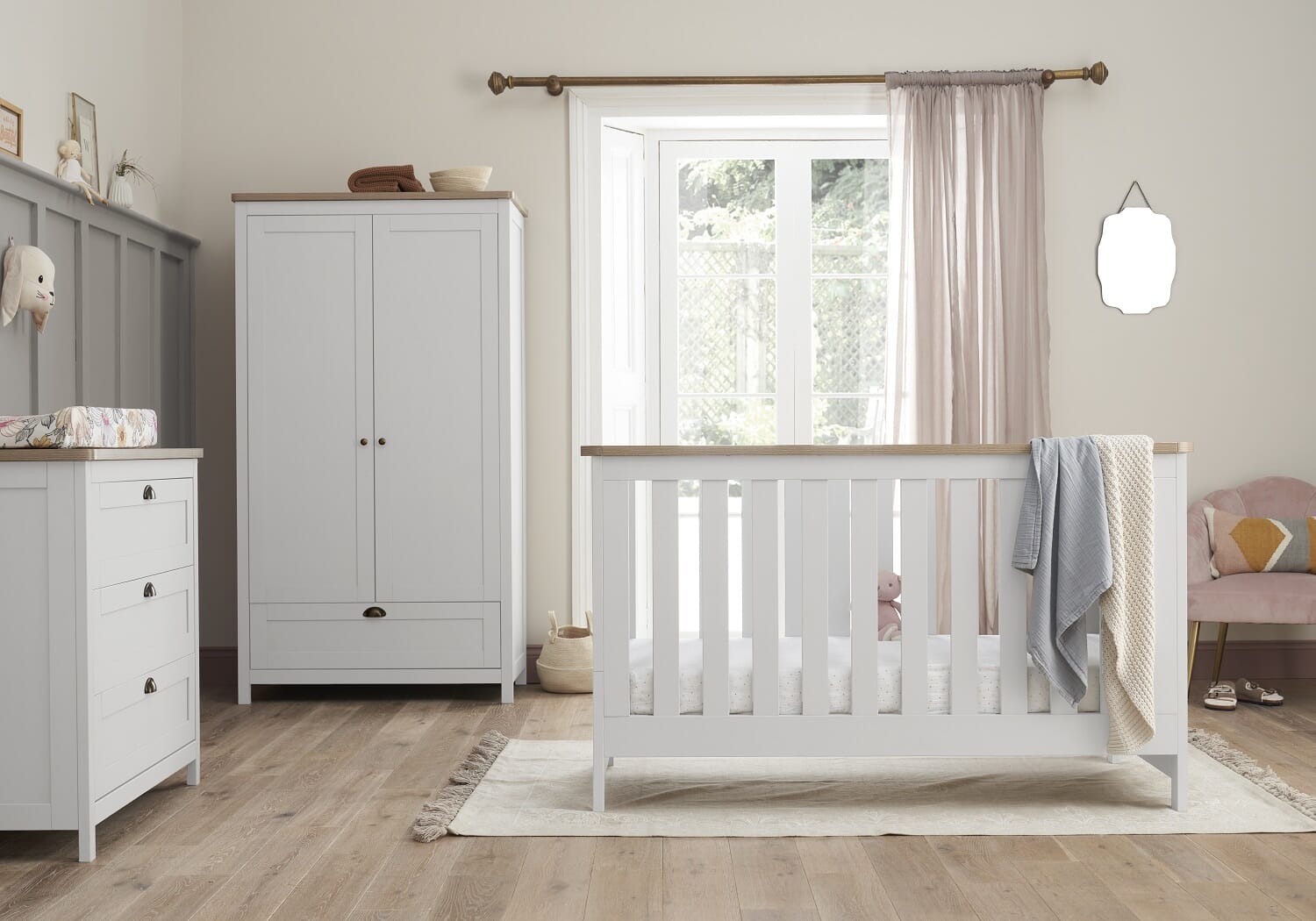 Bright nursery scene with the Verona cot bed, wardrobe and chest changer in white and oak, styled with soft textiles and warm natural light.