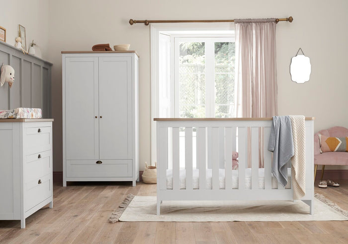 Bright nursery scene with the Verona cot bed, wardrobe and chest changer in white and oak, styled with soft textiles and warm natural light.
